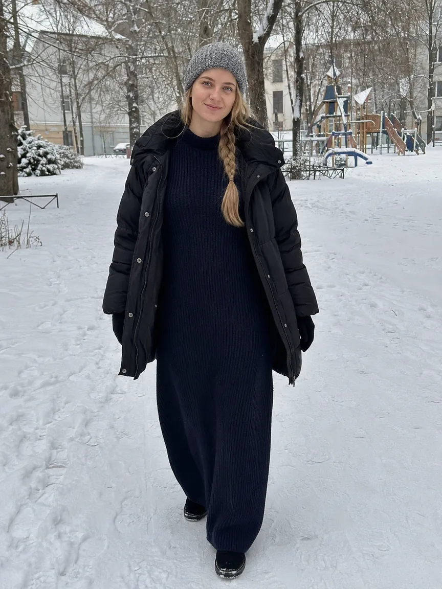 Женщина в пуховике и утеплённых ботинках с платьем макси идёт по снегу